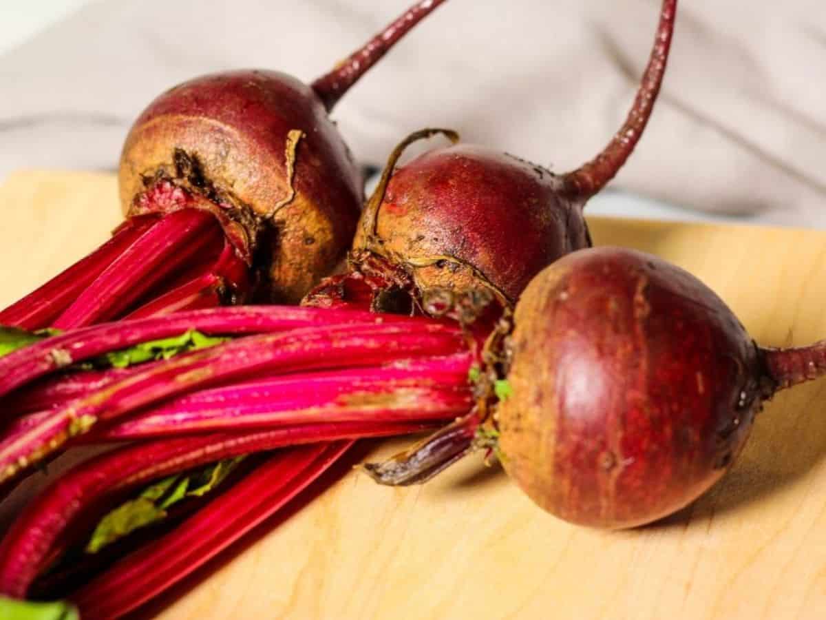 Three raw medium beetroots with greens attached on a cutting board.