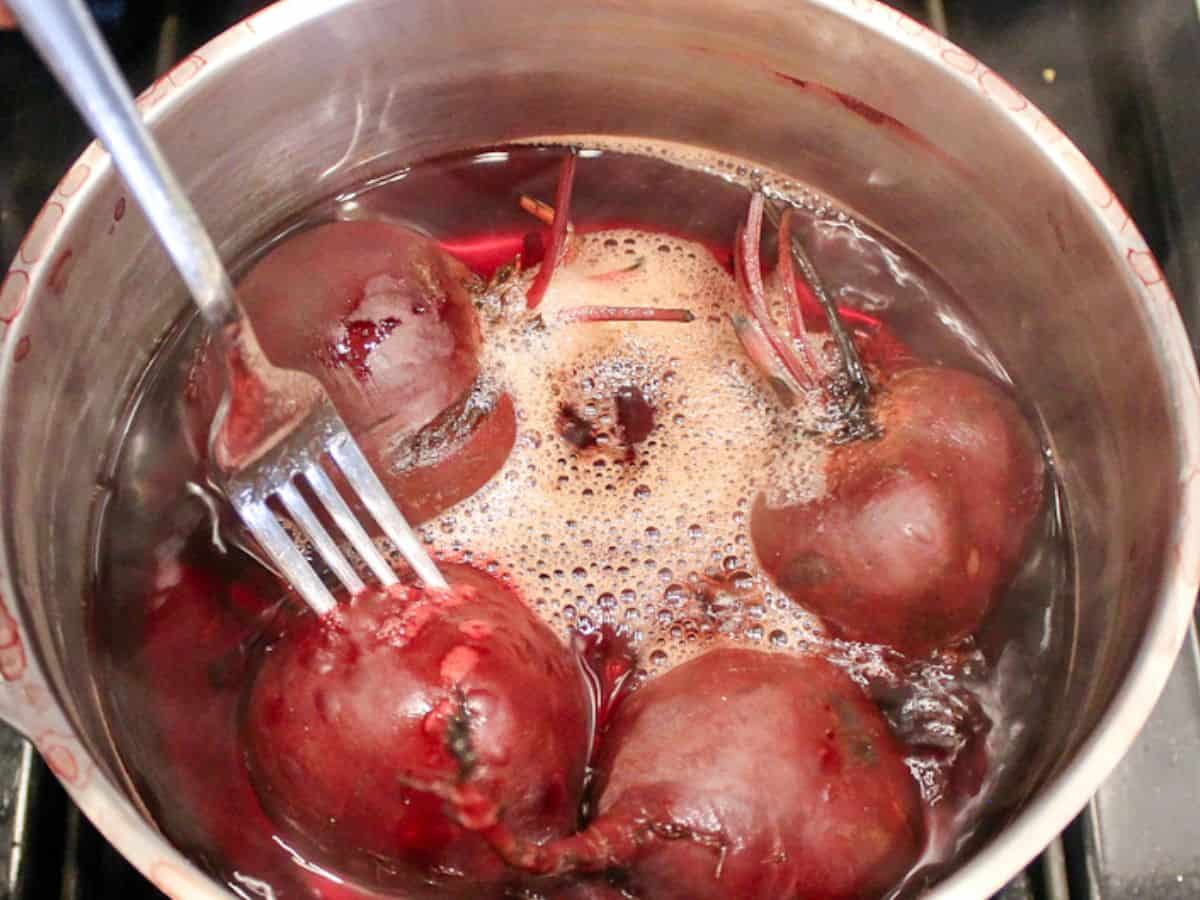 A fork pierced in one of the cooked beets in a pot with steamy water.