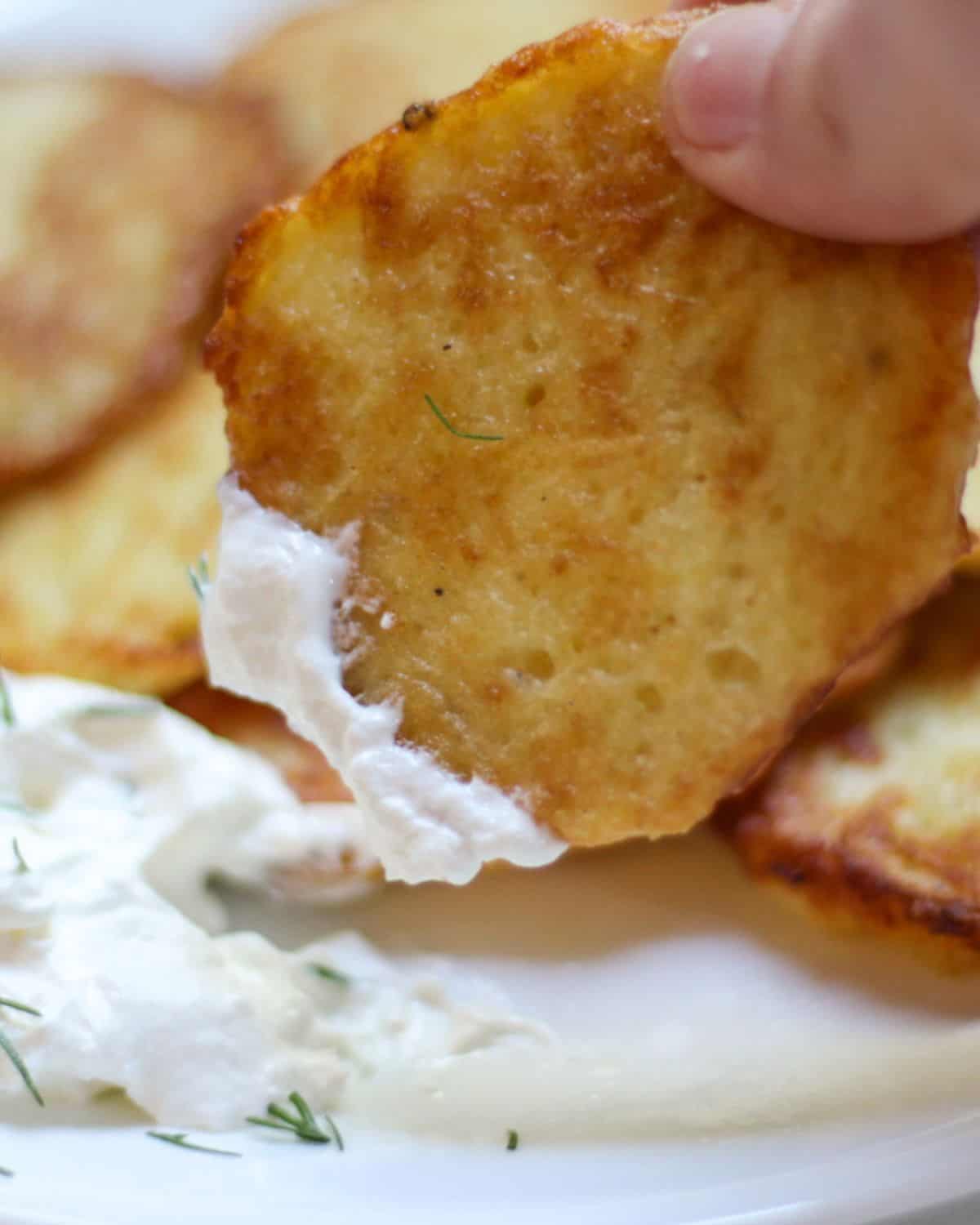 Golden potato pancake being dipped in sour cream.