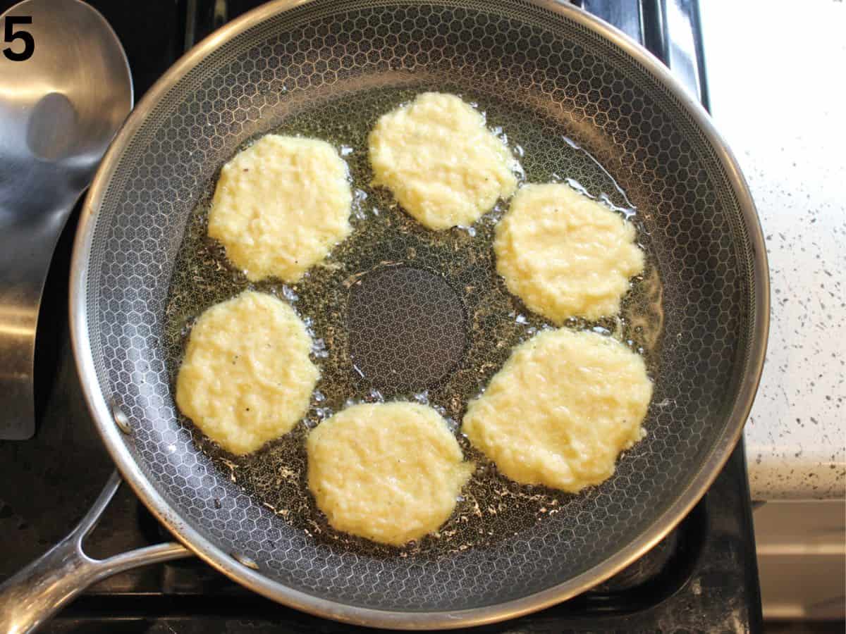 Potato pancakes frying in oil in a frying pan.