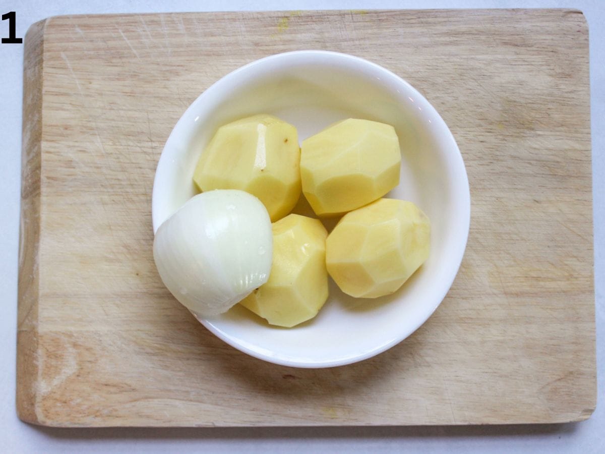 Peeled potatoes and one onion in a white bowl.