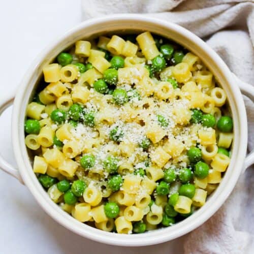 Ditalini pasta and green peas dish with grated Parmesan on top in a white bowl.