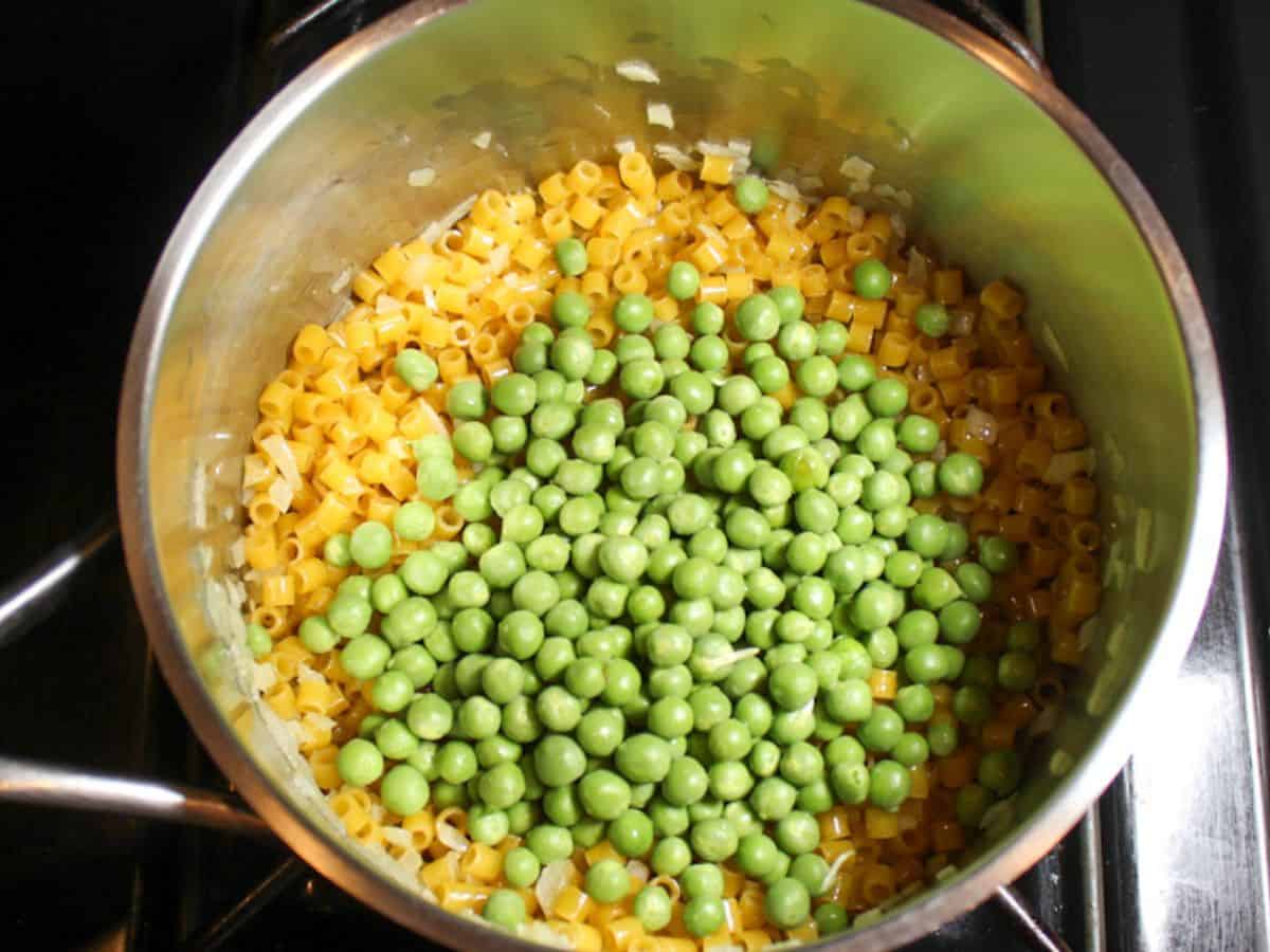 Fresh green peas added to the pasta in a pot.