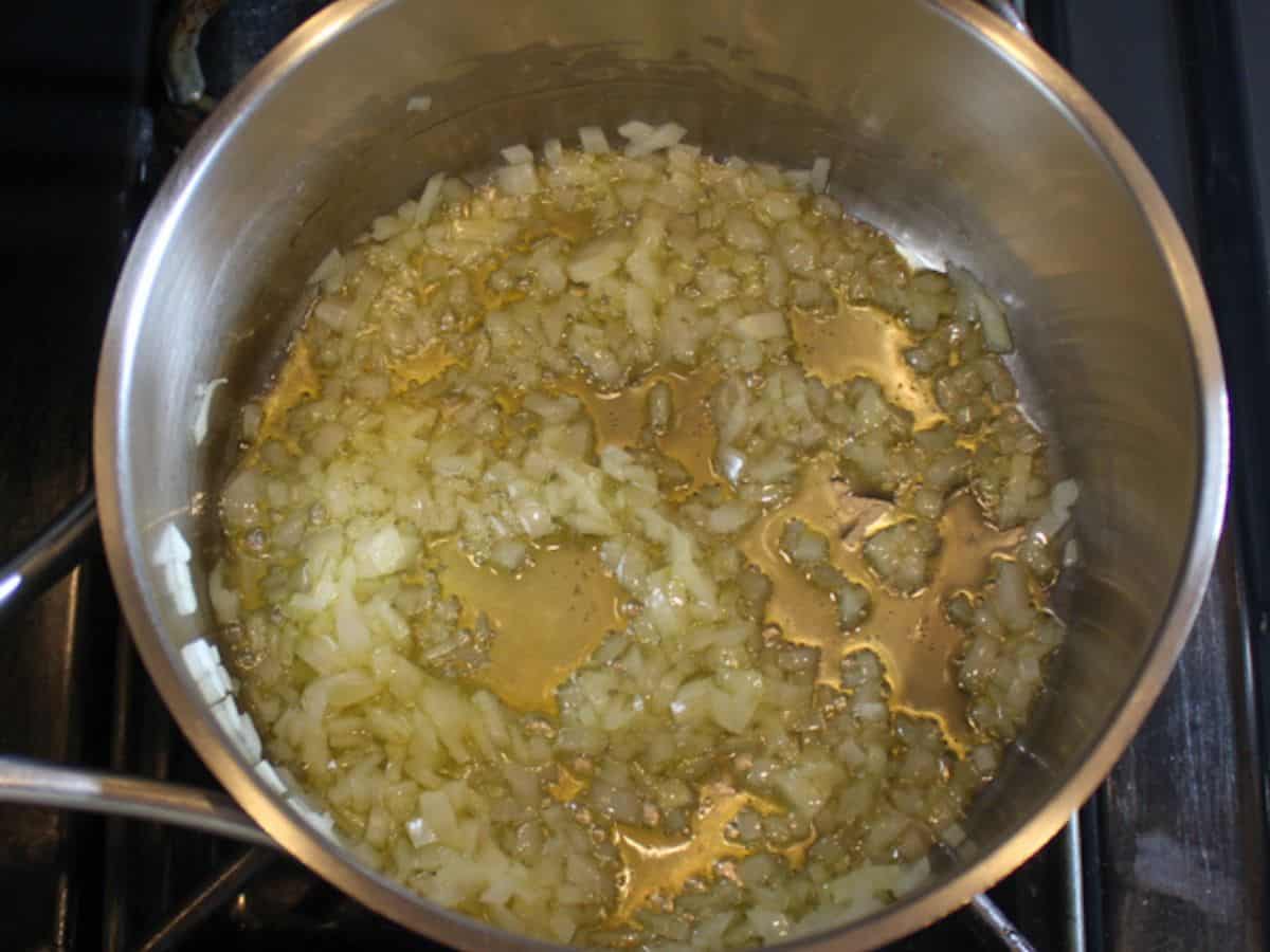 Finely diced onion sauteing in a stainless steel pot.