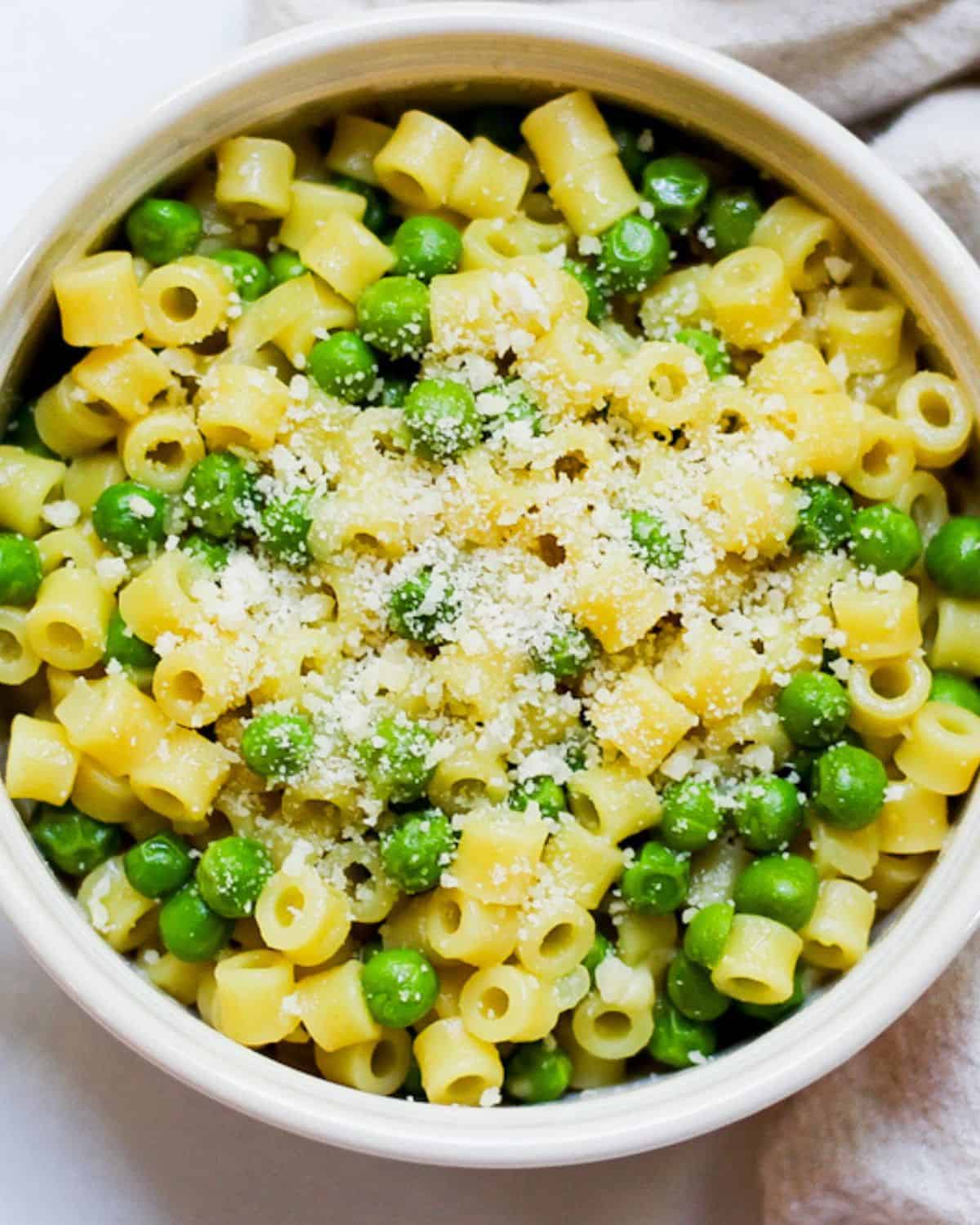 Ditalini pasta and green peas dish with grated Parmesan on top in a white bowl.