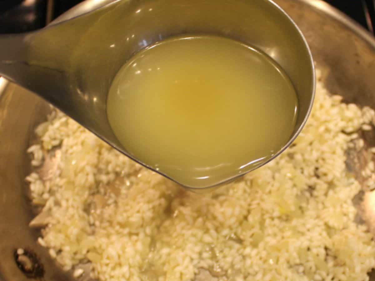 A ladle filled with broth over the pan with risotto rice.