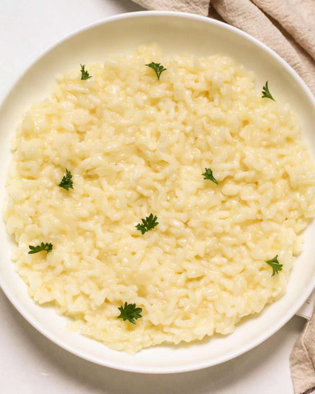 Parmesan risotto plated in a shallow dish and garnished with fresh green parsley leaves.