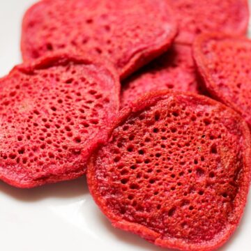 Pink beet pancakes piled on a white plate.