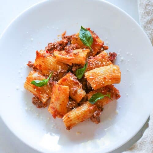 Baked Rigatoni pasta with tomato meat sauce on a white plate garnished with fresh basil leaves.