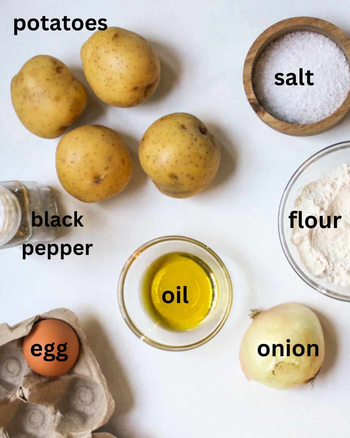 Labeled recipe ingredients on a white surface: golden potatoes, onion, egg, flour, black pepper, salt, and oil.