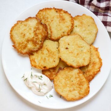 Deruny potato pancakes on a white place served with a dollop of sour cream.