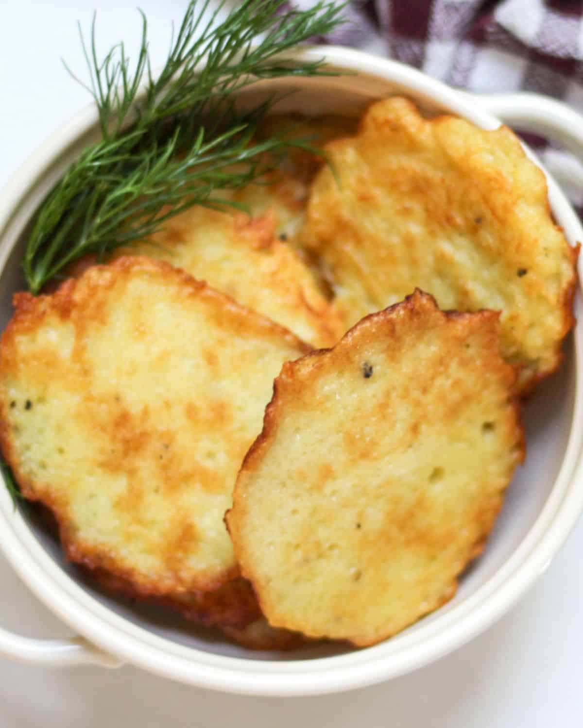 Deruny piled in a bowl with some green dill on a side.