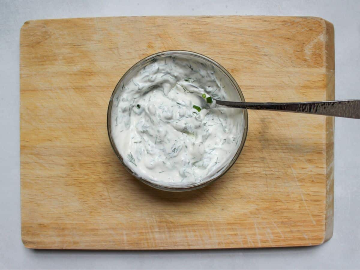 White creamy dressing with chopped dill in a bowl with a spoon in it.