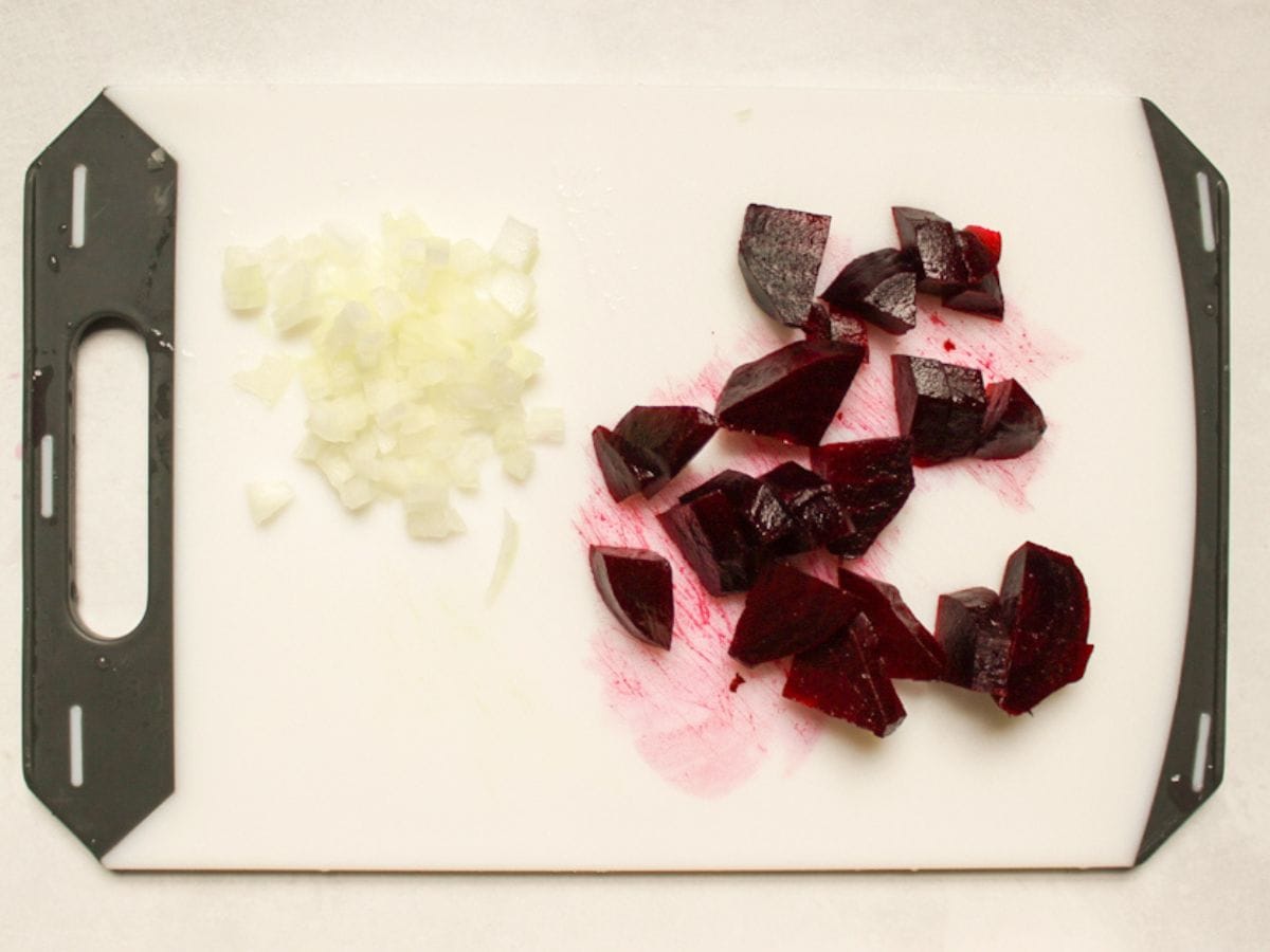 Finely diced onion and roughly chopped cooked red beet on a white cutting board.