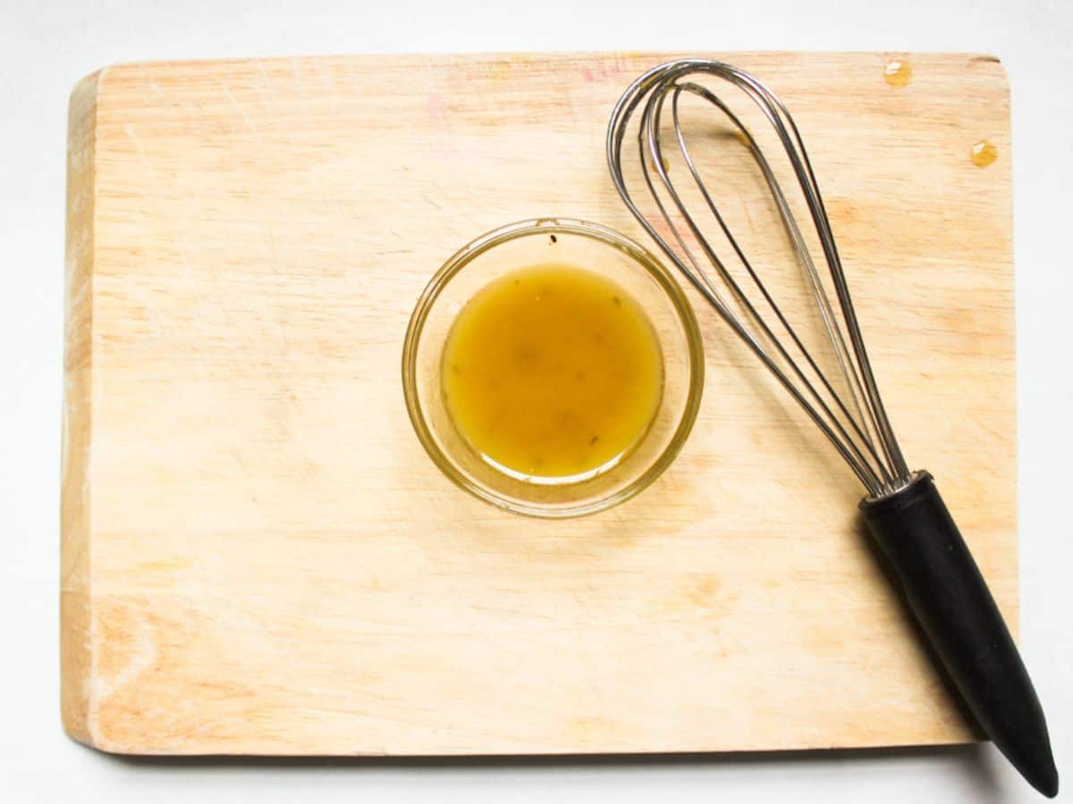 The emulsion with oil and vinegar in a small glass bowl. There is a whisk next to the bowl.