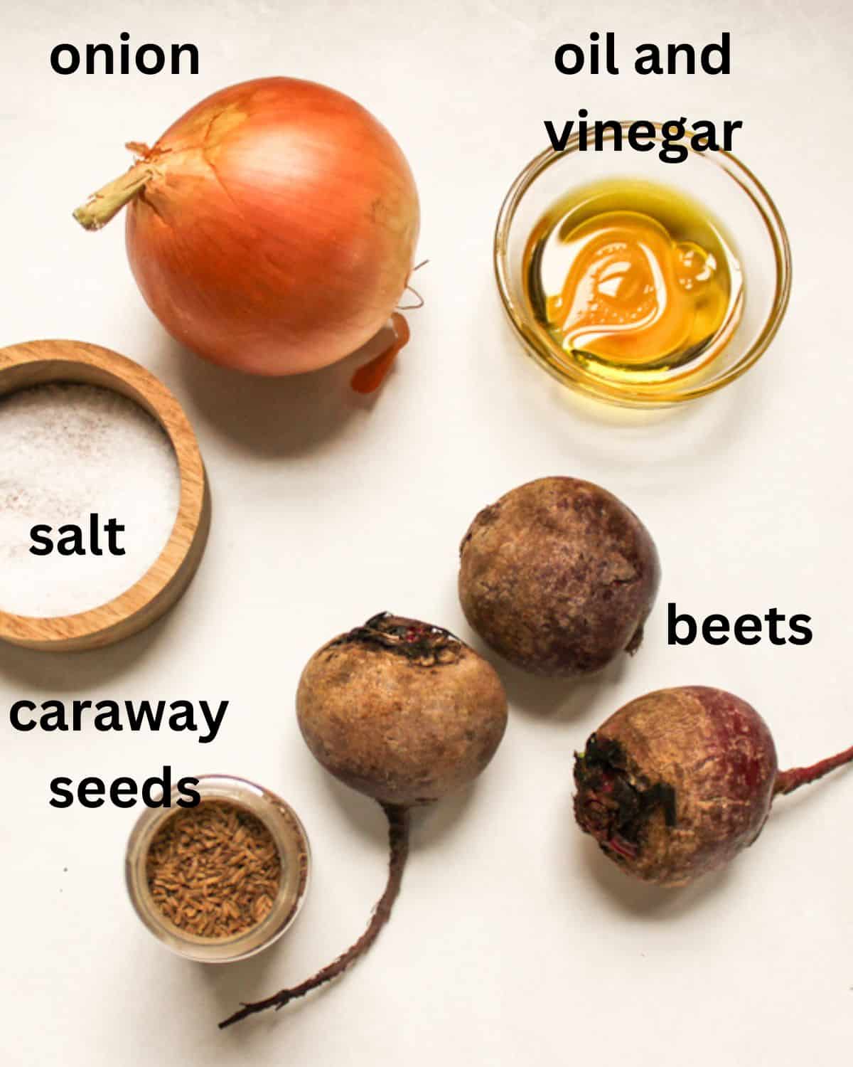 German beet salad ingredients on a white background labeled as onion, vinegar, oil, beets, salt and caraway seeds.