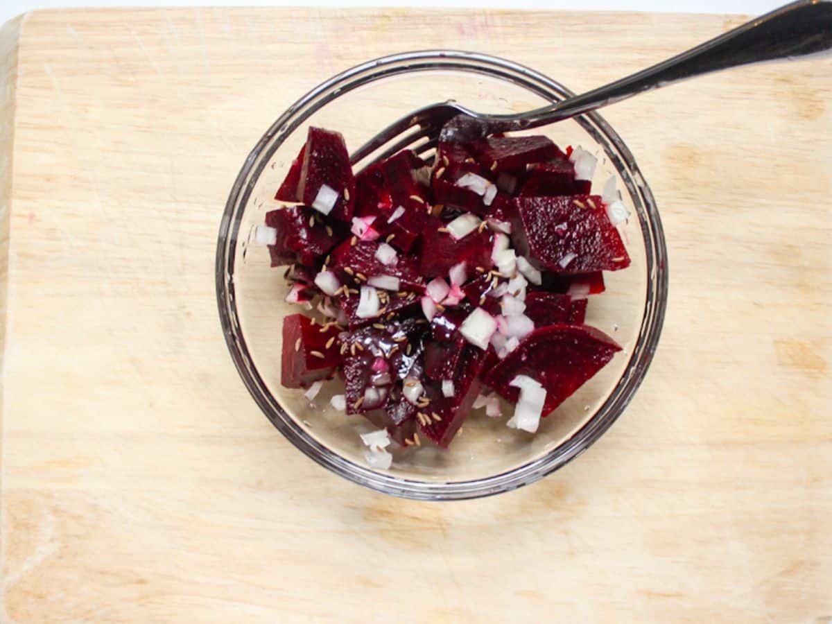 A glass bowl with red beet pieces and diced onion.