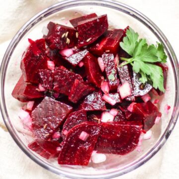 Rote Beete salat made with cooked red sliced beets, finenly diced onion and garnished with a green parsley leaf in a glass bowl.