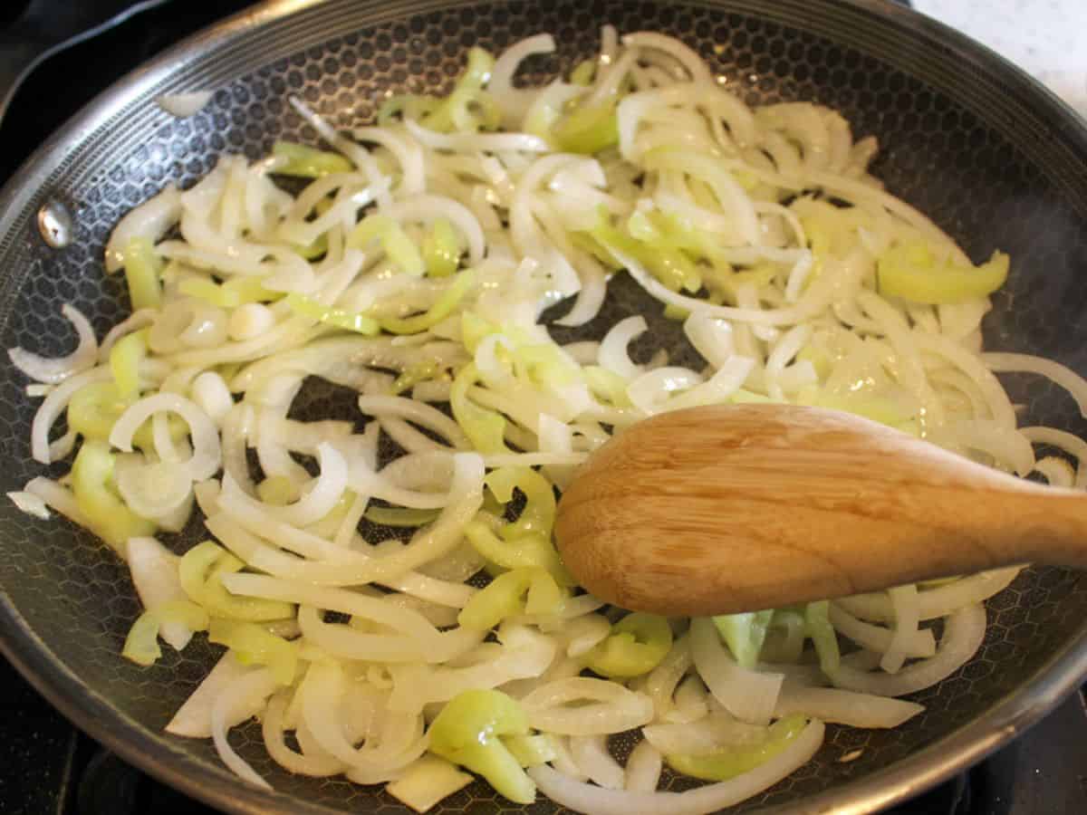 Sliced onions and green pepper sauteing in a large skillet