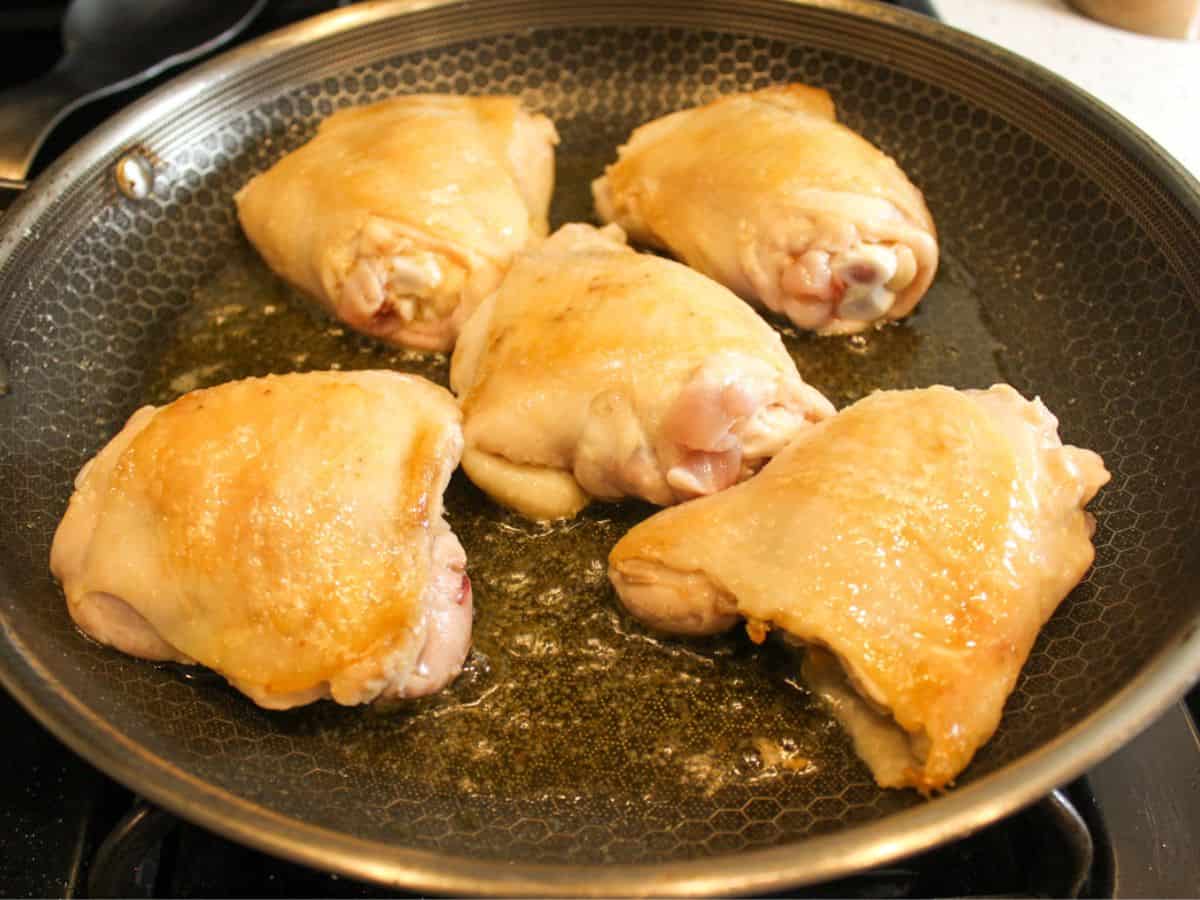 Skin-on chicken thighs searing in a skillet.