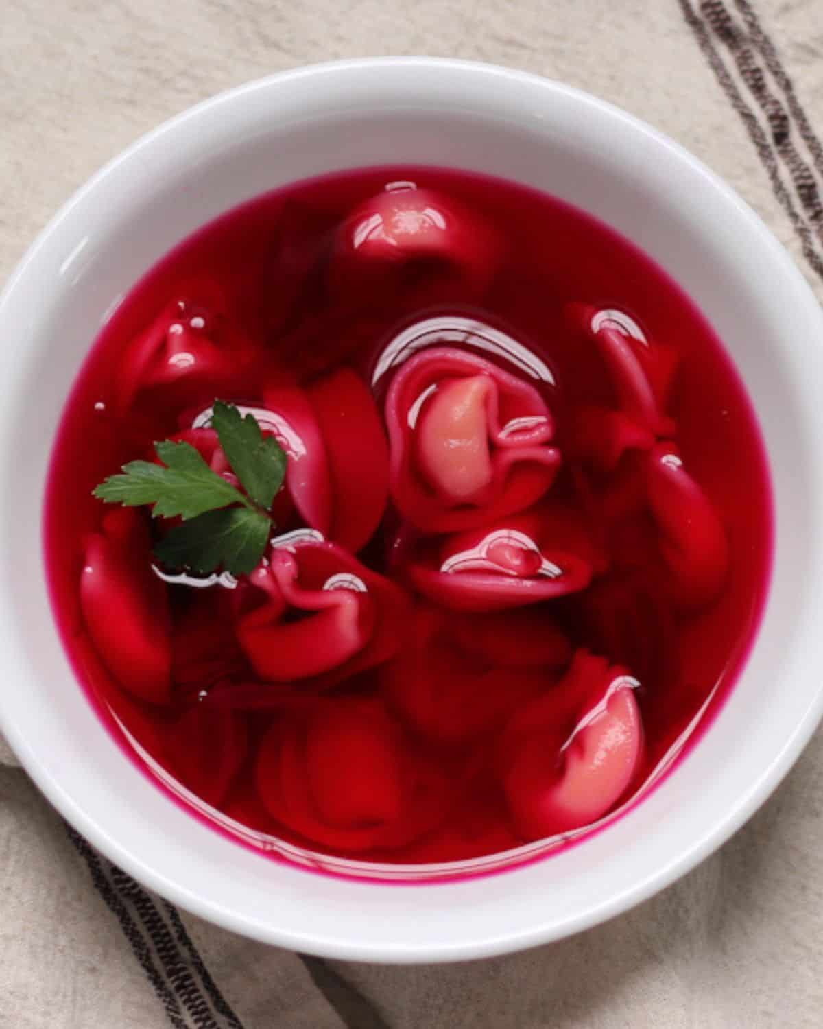 Polish red borscht with mushroom dumplings in a white bowl garnished with some fresh green parsley on top. 