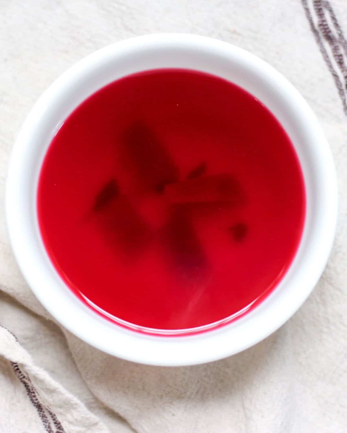 Clear Polish red borscht in a white bowl with a a few vegetable pieces visible at the bottom.
