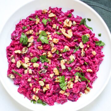 Turkish beet salad with yogurt topped with green parsley and walnuts in a large white plate.