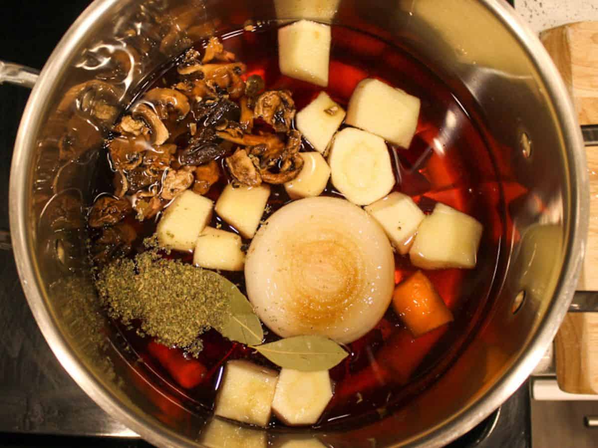 Half of the onion, soaked dried mushrooms, bay leaves, marjoram, carrots and parsnip are added to the pot.