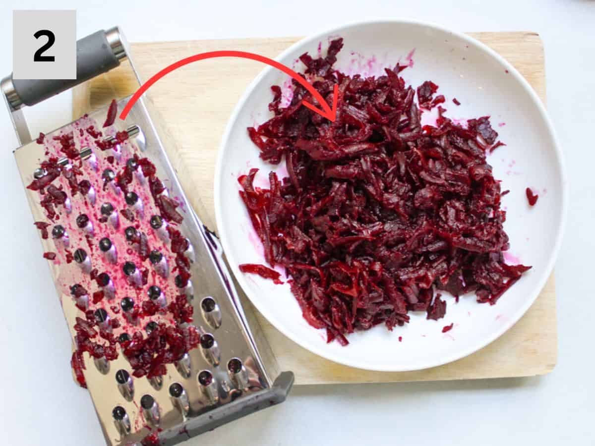 Grated red beets in a plate with a box grater next to it on a wooden cutting board,