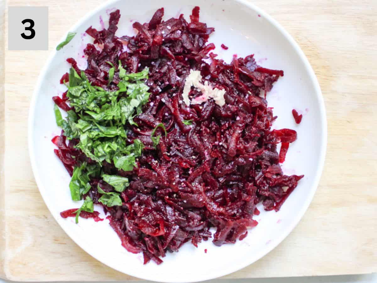 Grated cooked beets with added green herbs and minced garlic in a white dish.