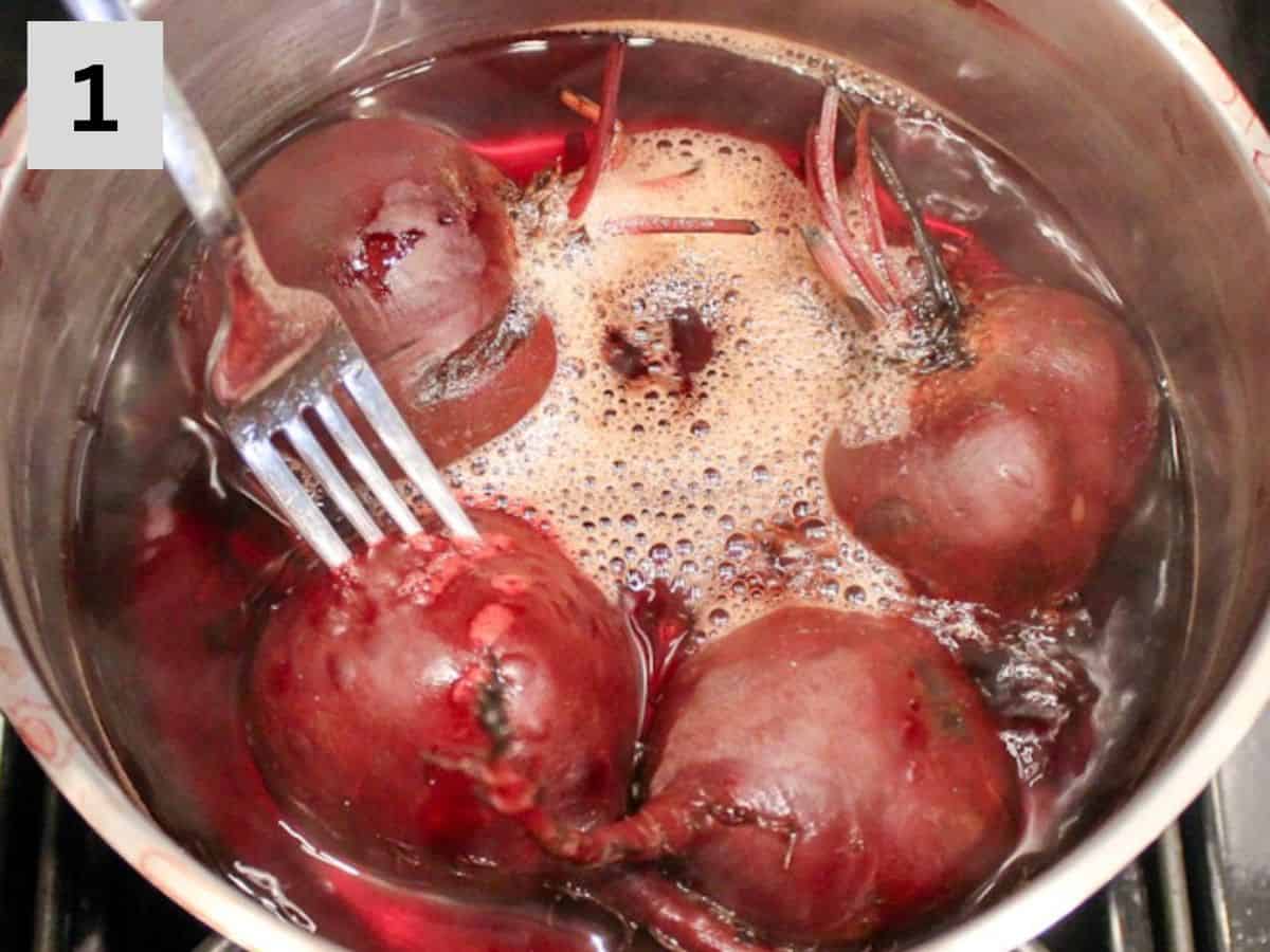 Boiling whole beets in a pot. The fork pierced in one of the beets.