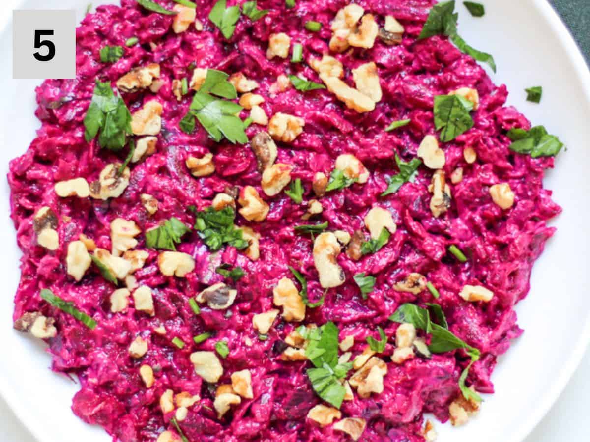 Roughly chopped green parsley and walnut pieces added on top of the beetroot salad in a white shallow dish.