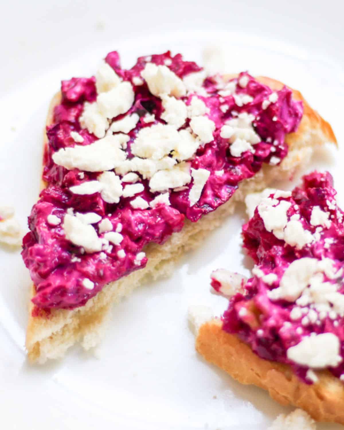 Grated beets salad spread on a bread and topped with crumbled feta cheese.