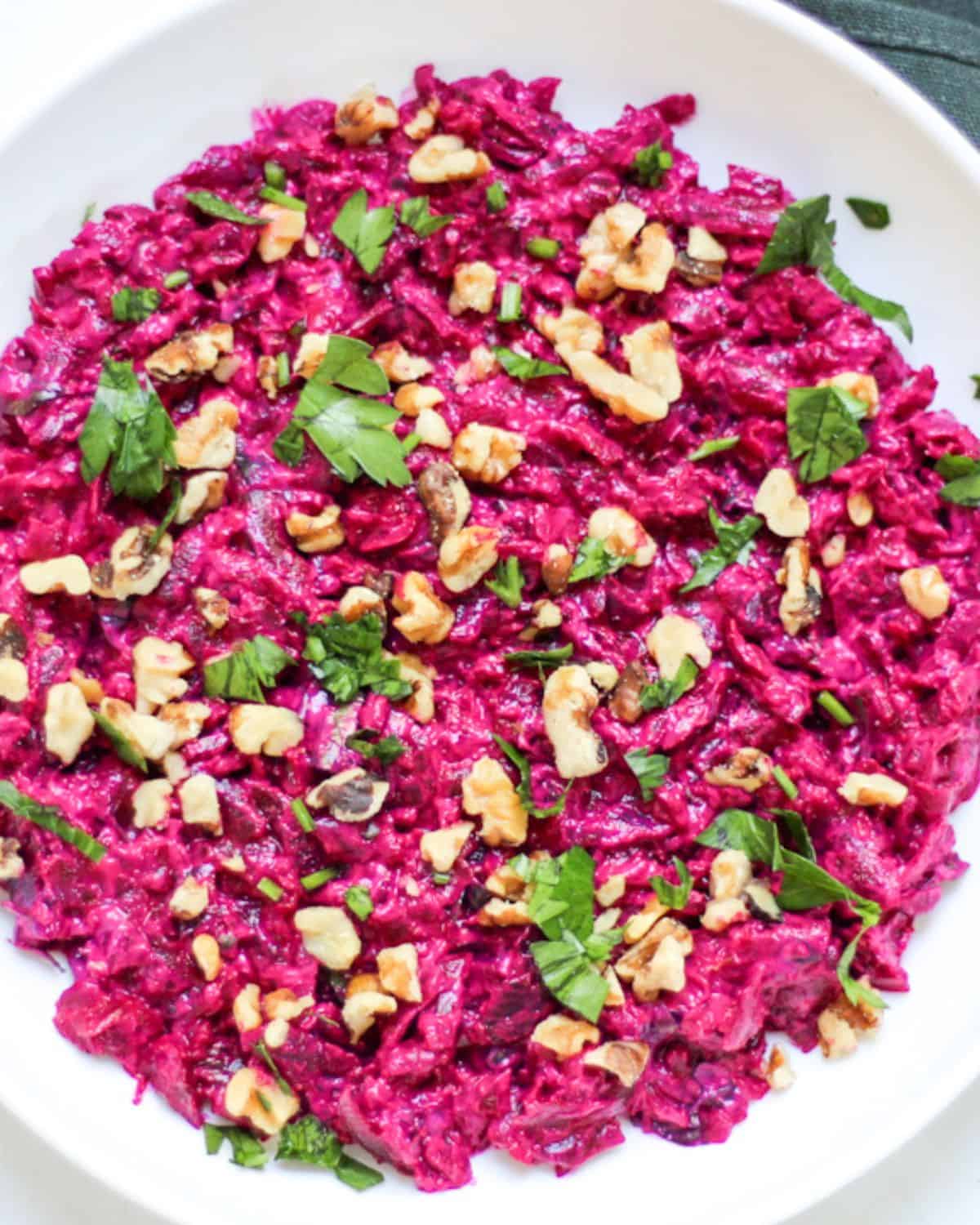 Turkish beet salad with yogurt topped with green parsley and walnuts in a large white plate.