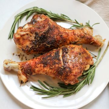 Two roasted turkey legs on a white dish with some two fresh sprigs of rosemary.