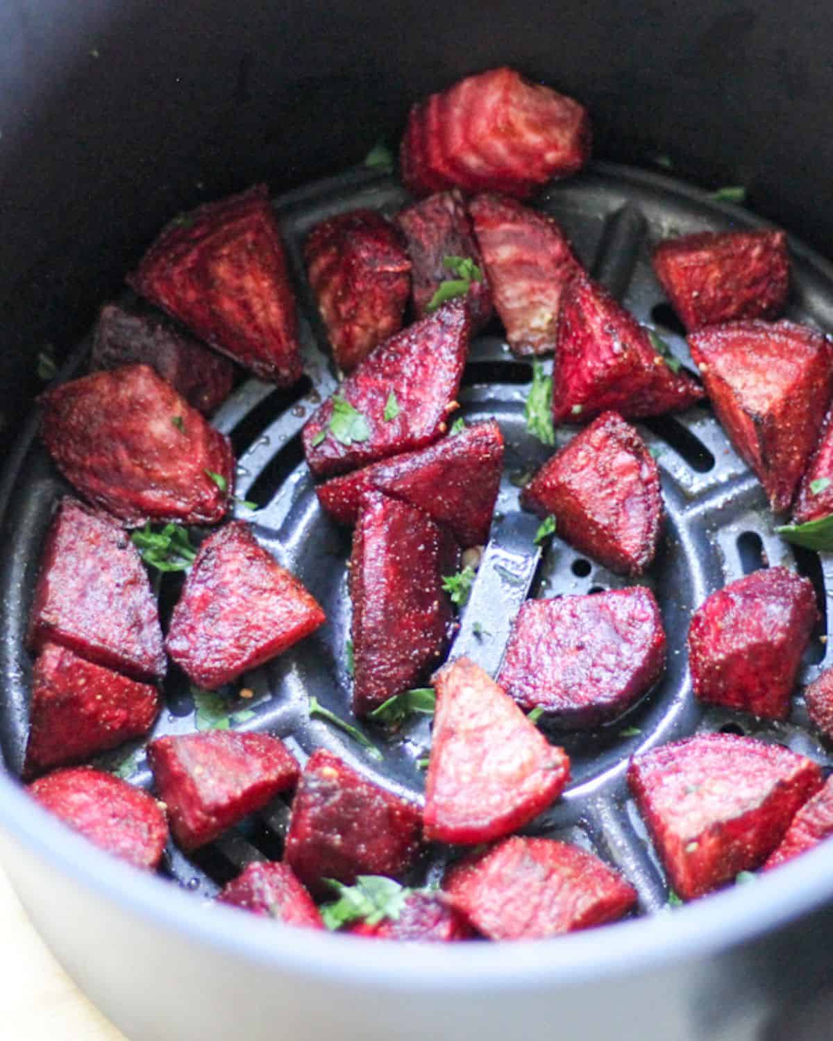 Roasted red beet pieces in air fryer basket with fresh parsley on top.