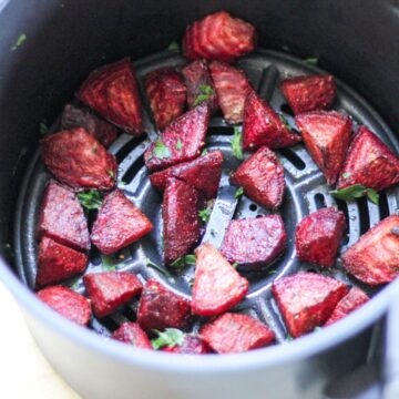 Roasted red beet pieces in air fryer basket with fresh parsley on top.