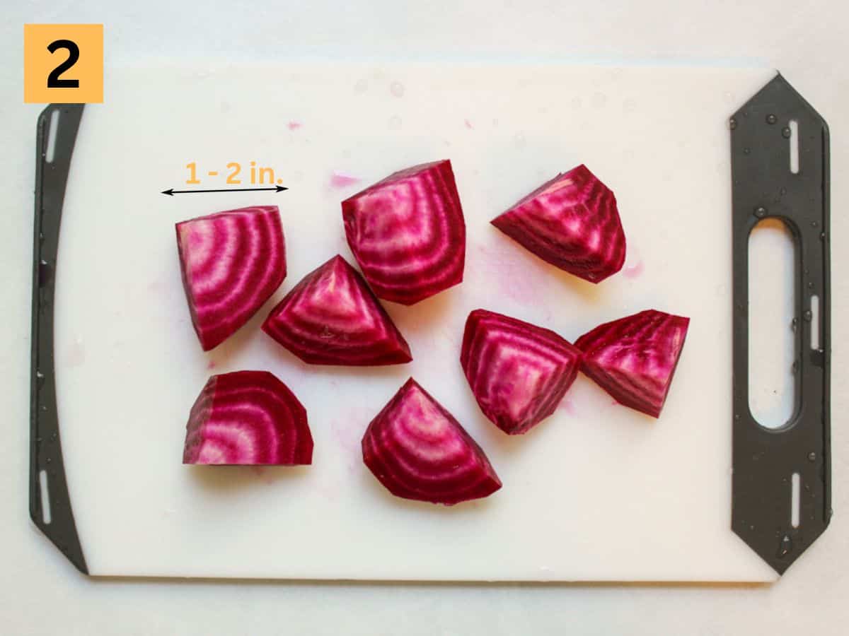 Raw beet pieces on a white plastic cutting board.