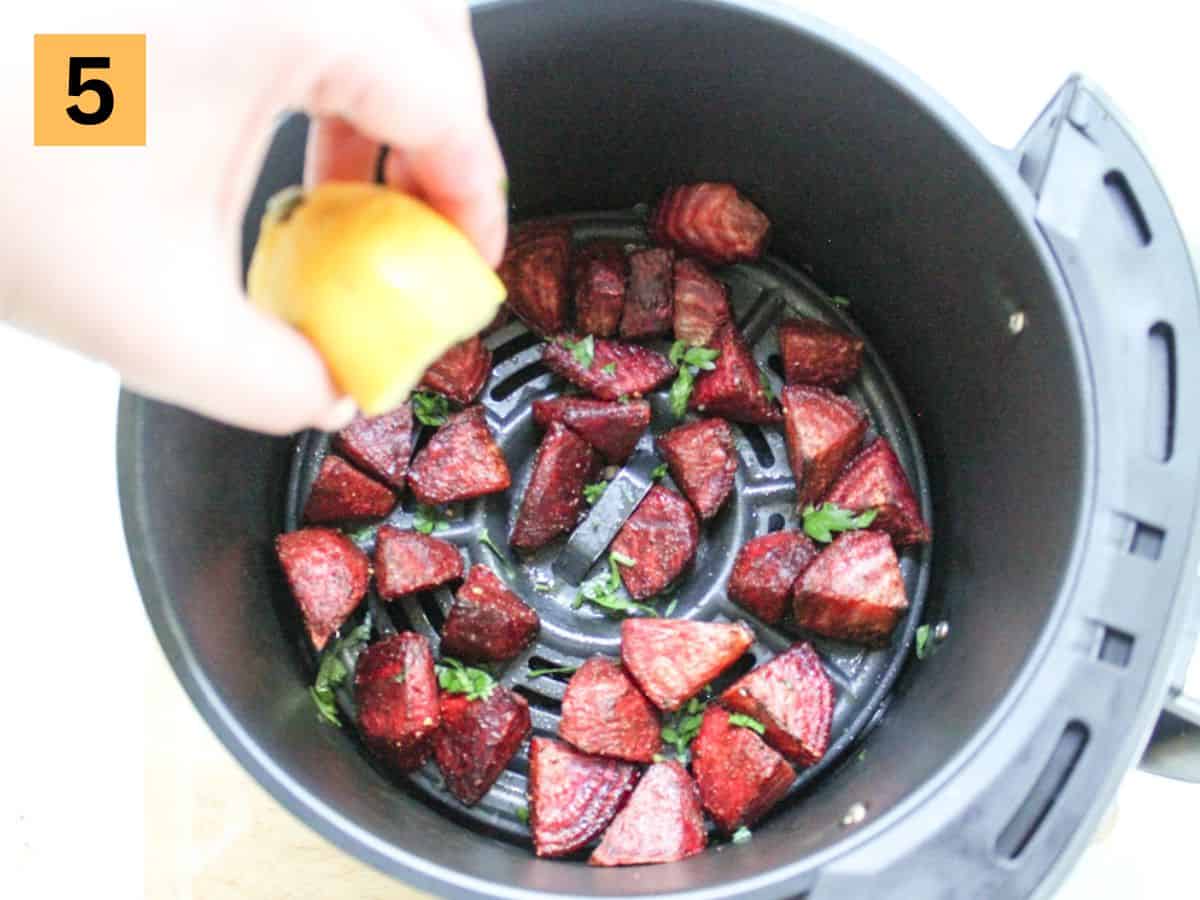 Half of the lemon being squeezed on top of the roasted beets in the air fryer basket.