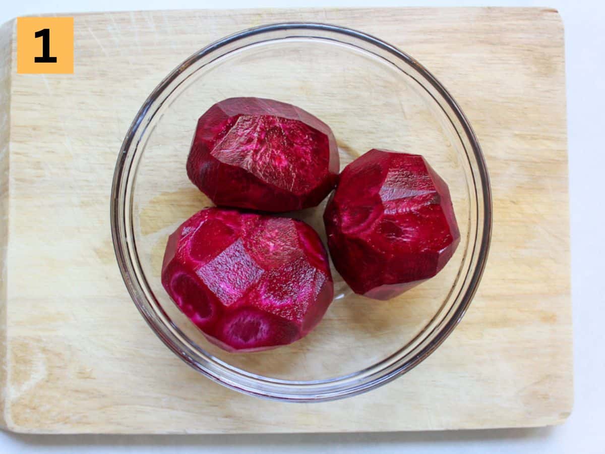 Three red peeled beets in a glass bowl.