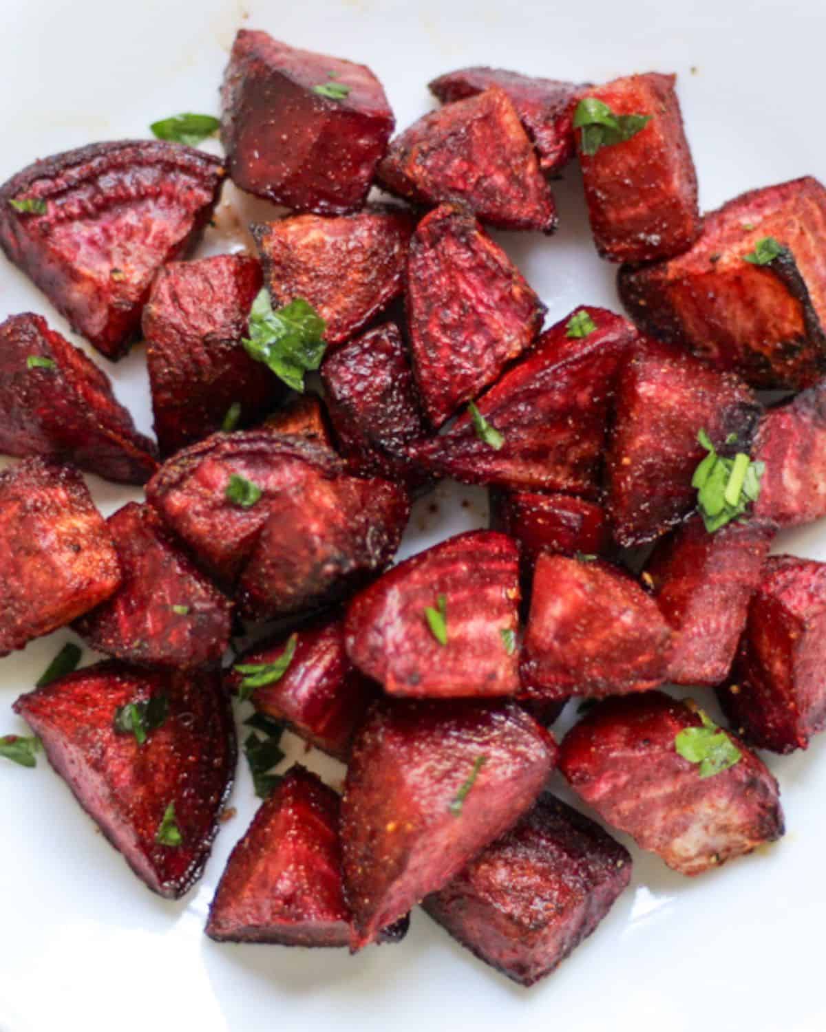 Roasted beets pieces sprinkled with fresh chopped green parsley on a white dish.