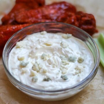 Creamy blue cheese dip in a glass bowl. There is buffalo wings and celery on the side of it.