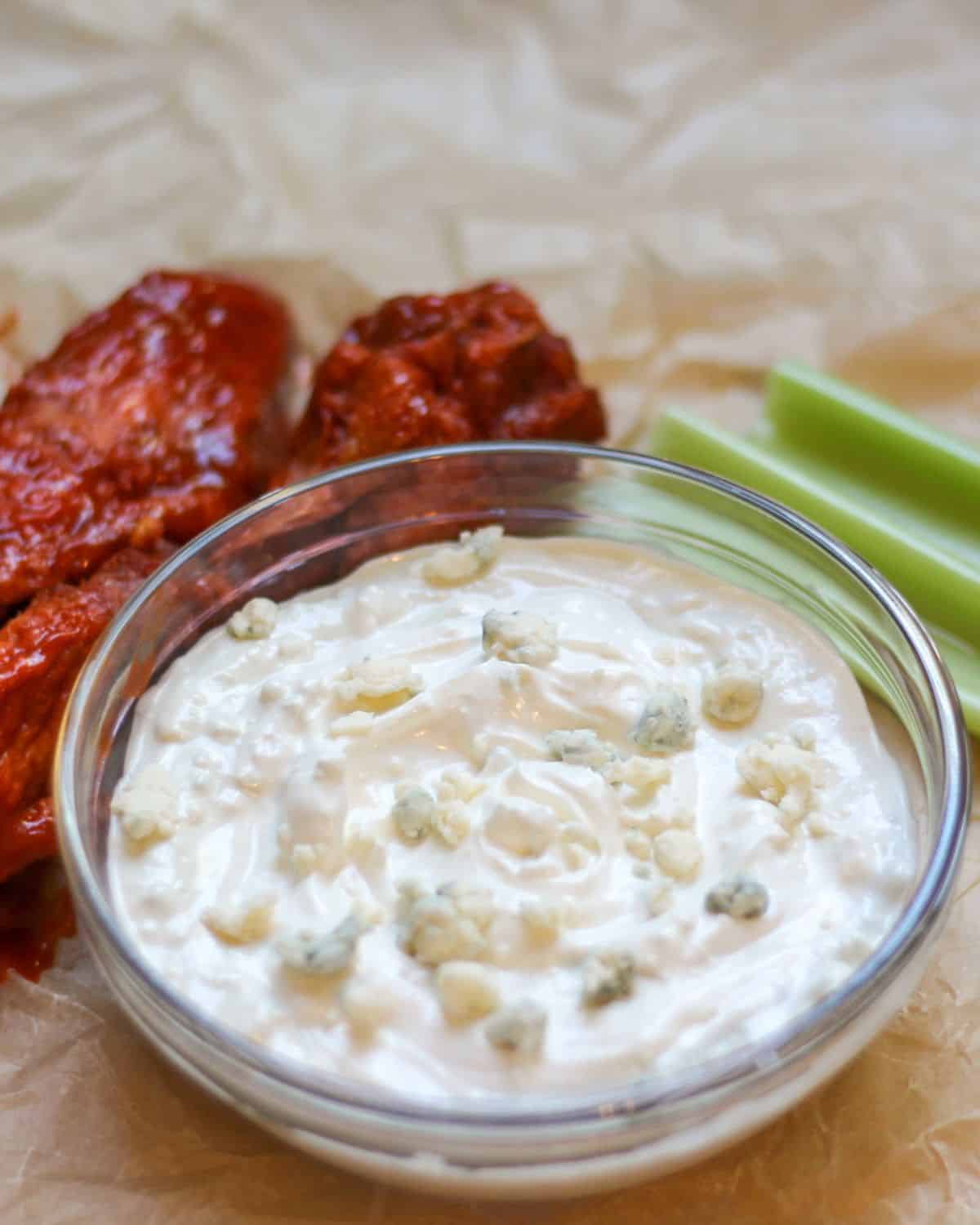 Creamy blue cheese dip in a glass bowl. There is buffalo wings and celery on the side of it. 