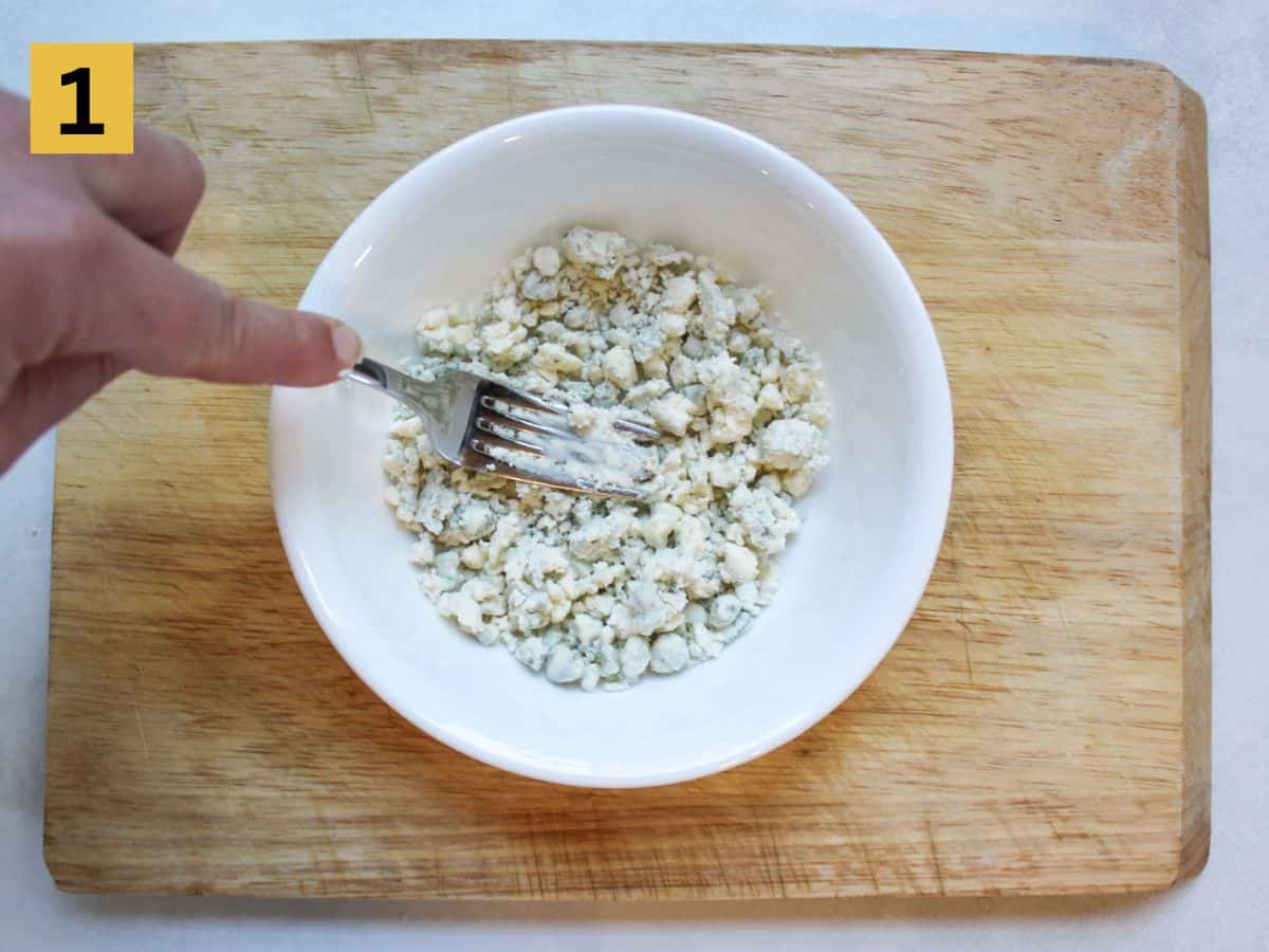 Blue cheese crumbled mashed with a fork in a white bowl.