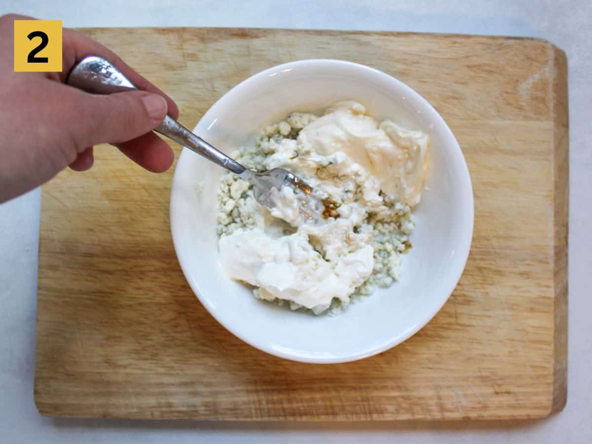 Blue cheese, sour cream, mayo and the rest of the dip ingredients are mixed in a white bowl.