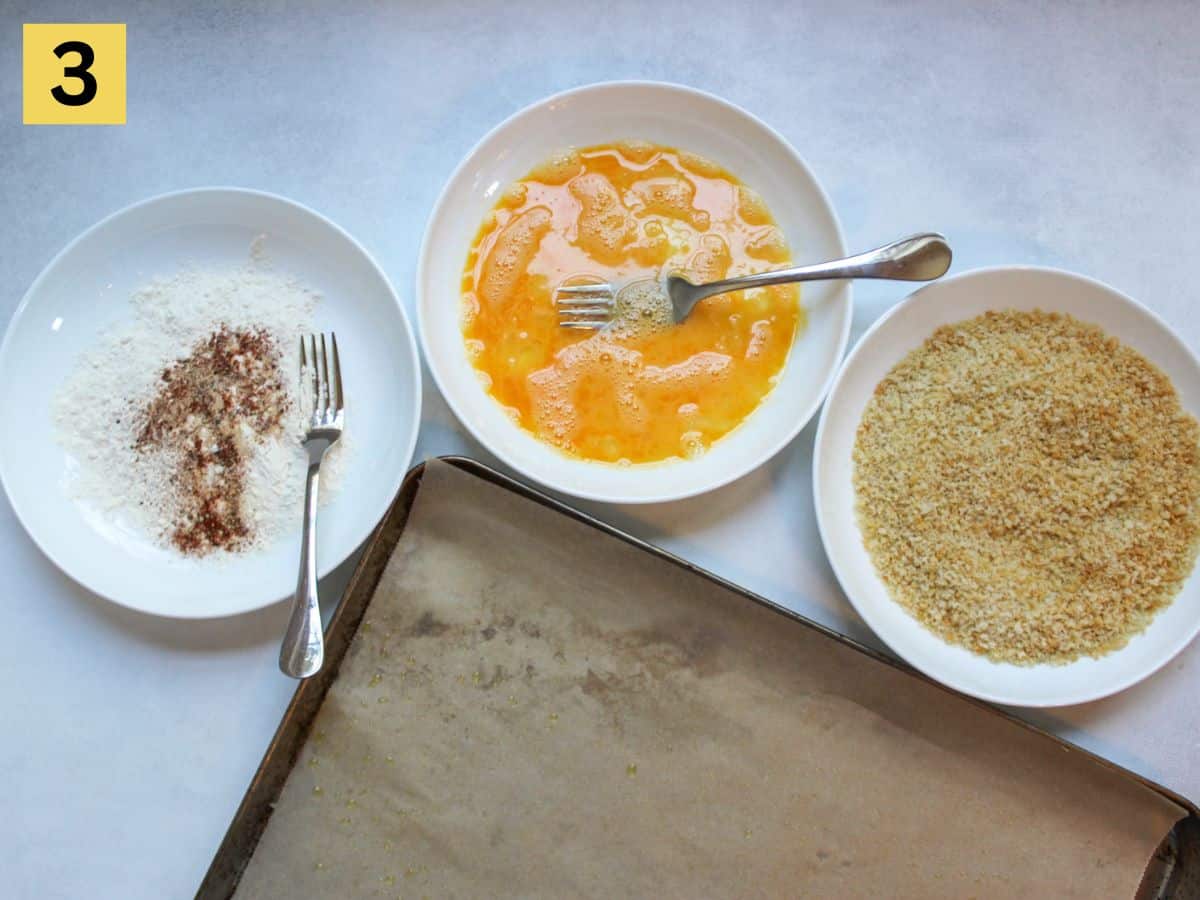 Step three. Three separate shallow white dishes: one with flour and spices. one with whisked eggs, one with toasted panko crumbs. There is a corner of baking pan lined with parchment paper at the bottom