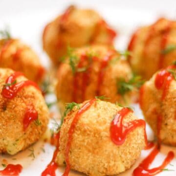 Mashed potato croquettes shaped as balls on a white plate drizzled with ketchup on top and sprinkled with fresh dill.