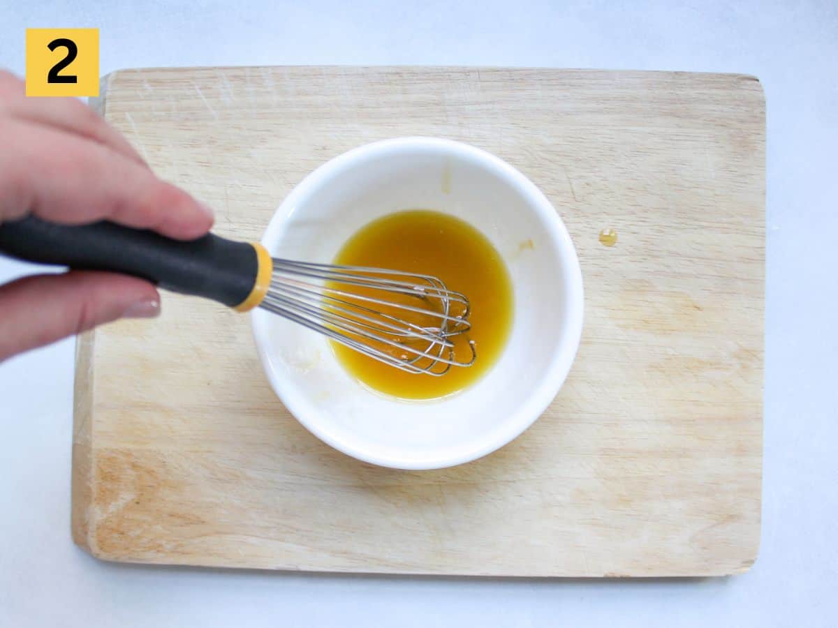 Salad olive oil and lemon dressing whisked in a small white bowl.