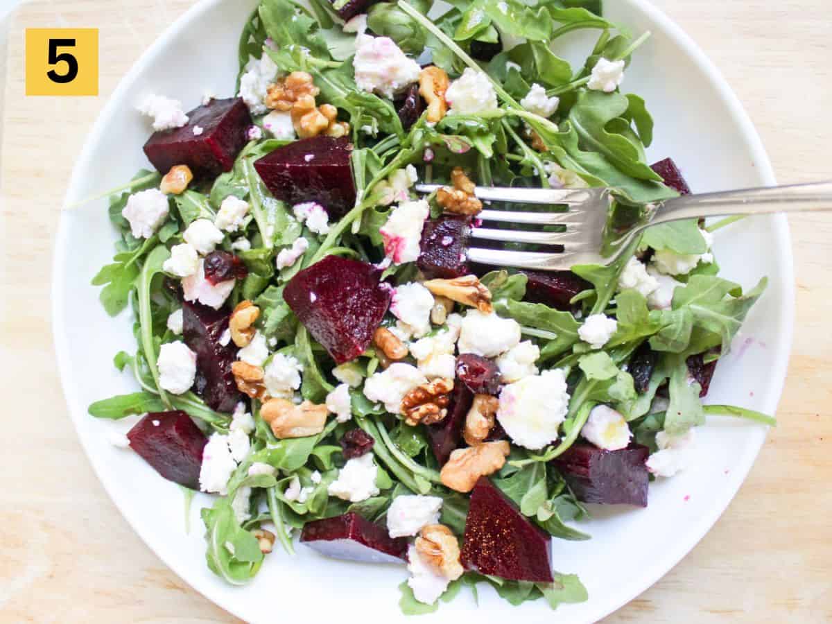 Arugula, beets and goat cheese salad topped with walnuts in a large white platter. 