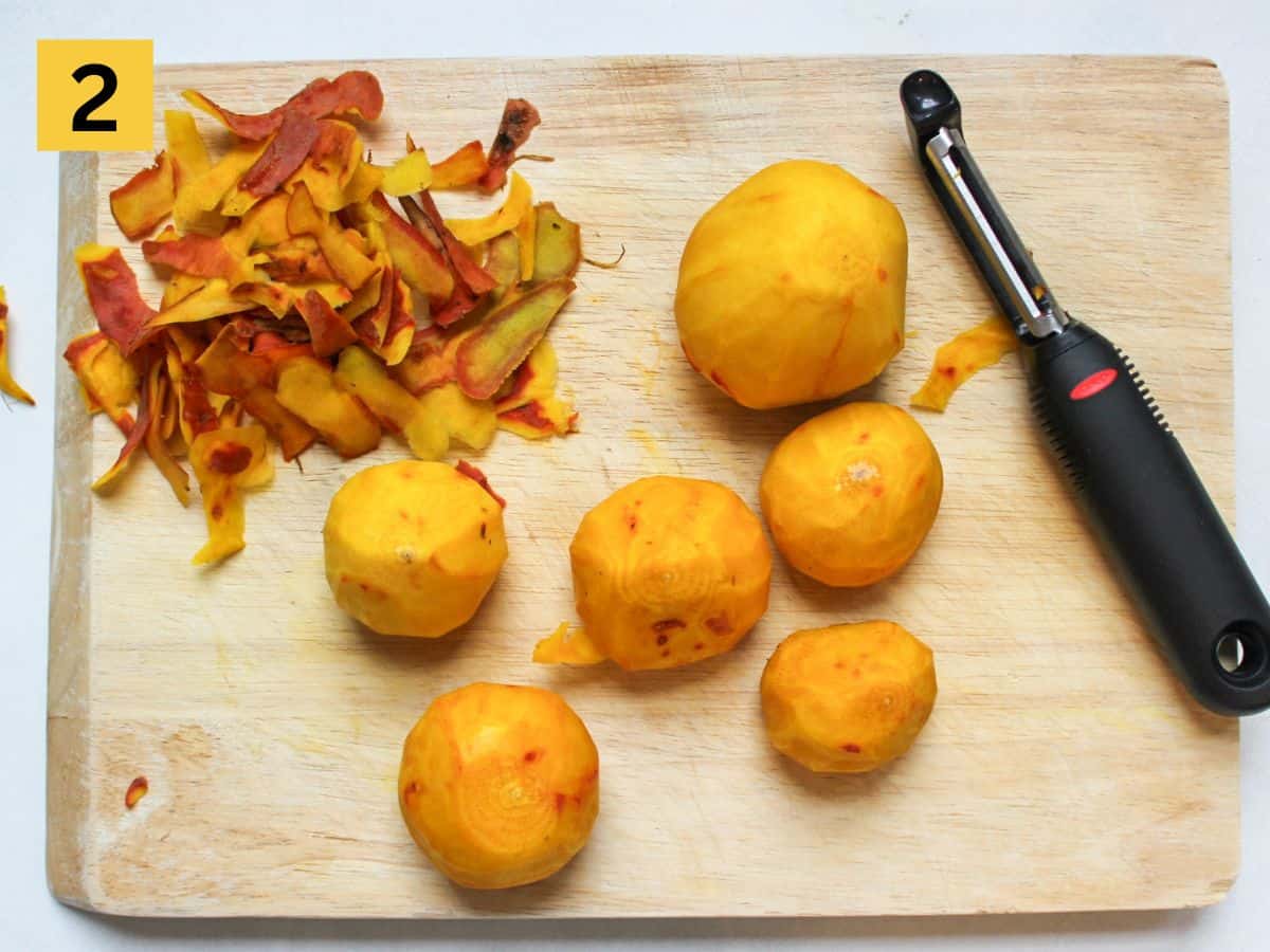 Peeled yellow beets on a cutting board with a veggie peeler on the side.